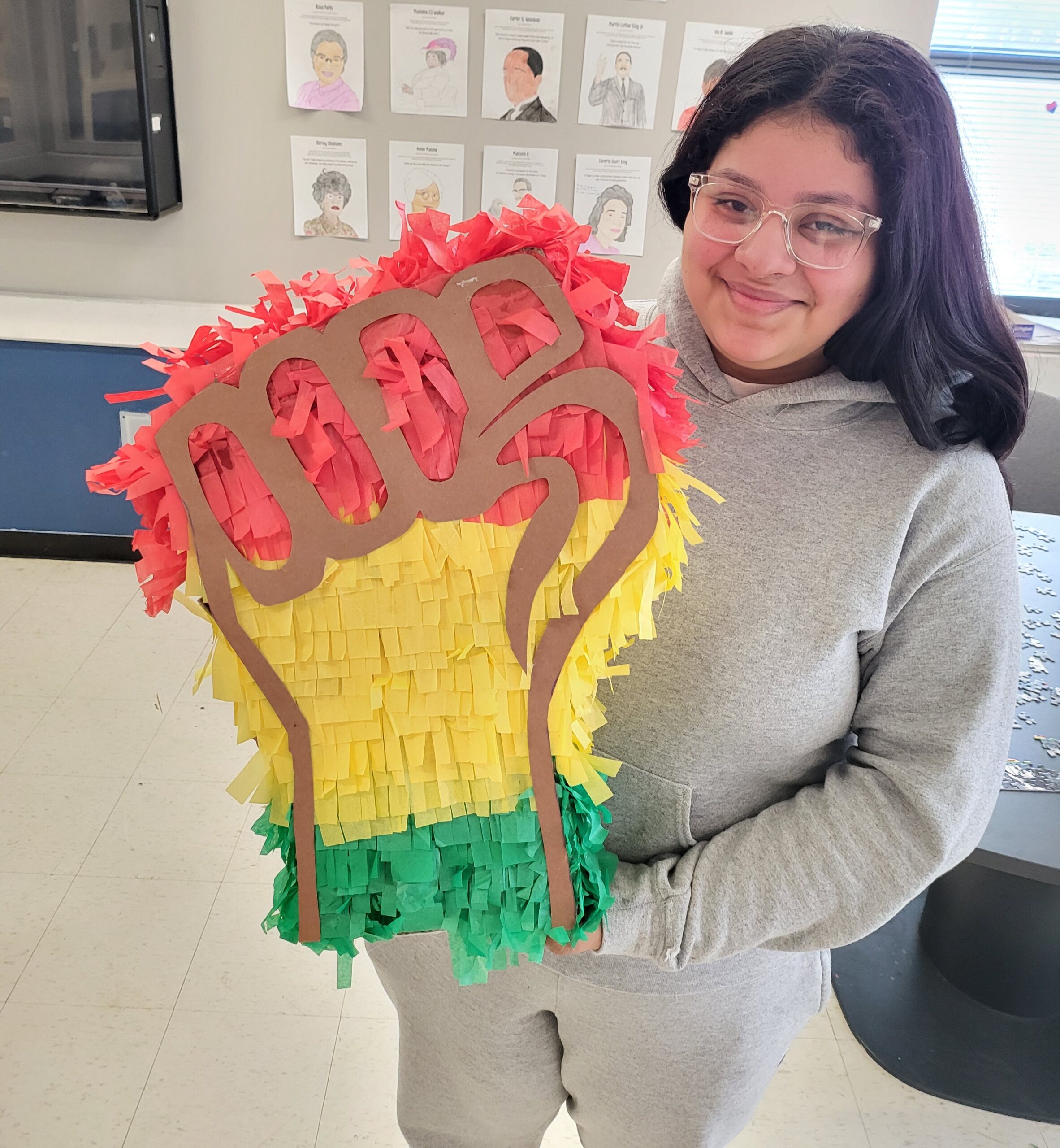 A young woman holds a pinanta of a fist in red, yellow, and green.