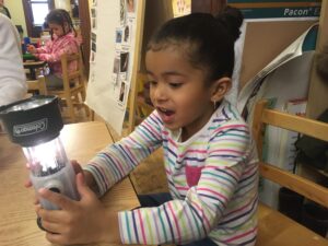 A girl turns on a flashlight and smiles.