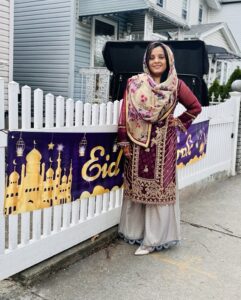 Mehak stands next to an Eid sign on a fence.