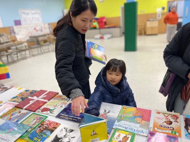 A child and her mom pick out a book from a display of books on a table.