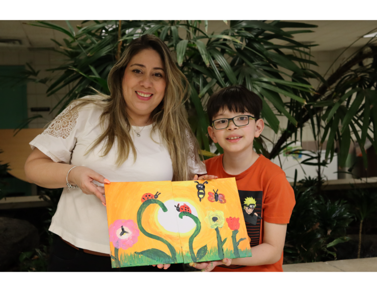 A mom and her third-grade son hold up a painting where there are two halves that make a whole.