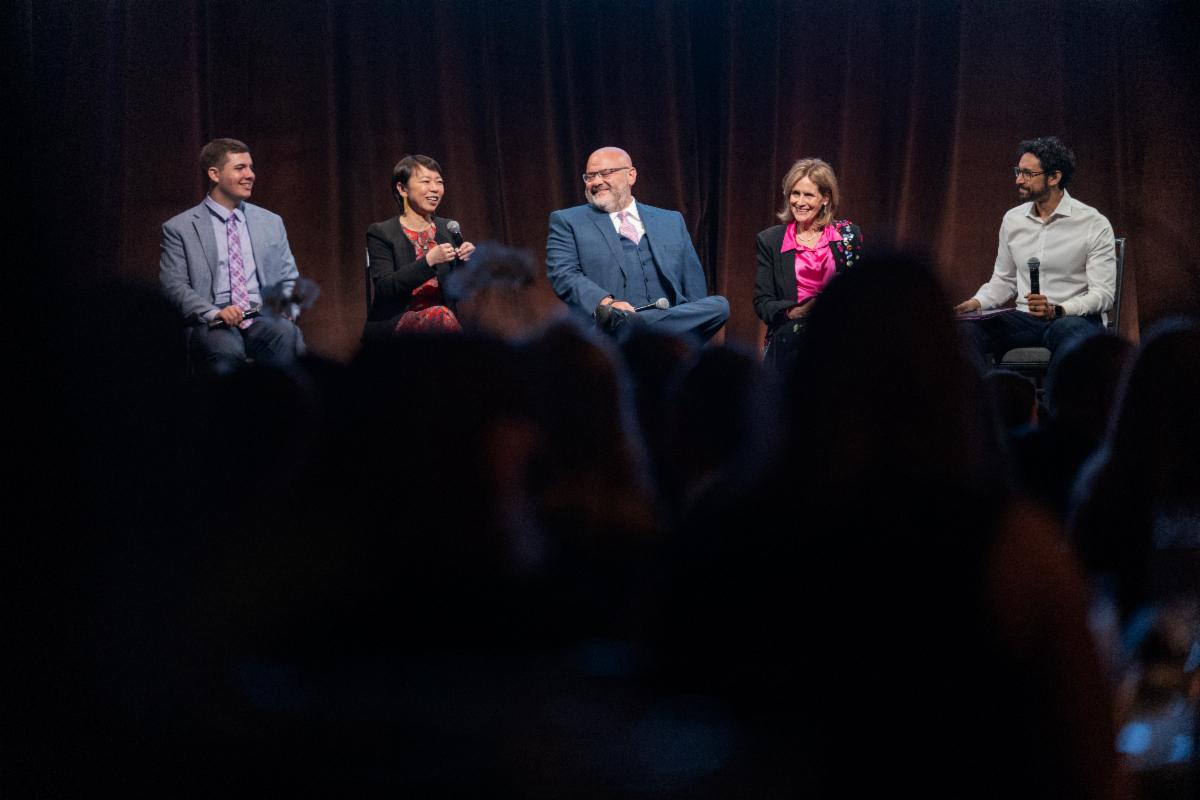 members of a panel sit in chairs on a dark stage.