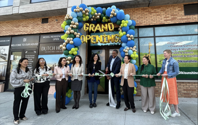 Several people stand in front of the balloon-decorated doors of Diki Sunshine daycare center and cut a ceremonial ribbon.