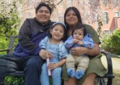 Guadalupe and her husband and two young sons sit on a bench outside.