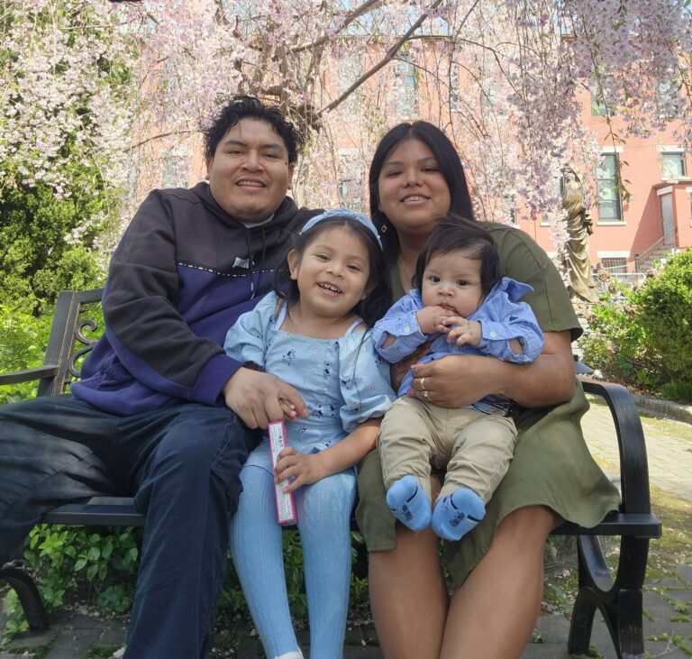 Guadalupe and her husband and two young sons sit on a bench outside.