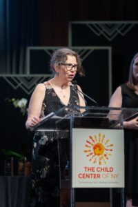 Tracey Elting speaks at a podium with the child center logo.