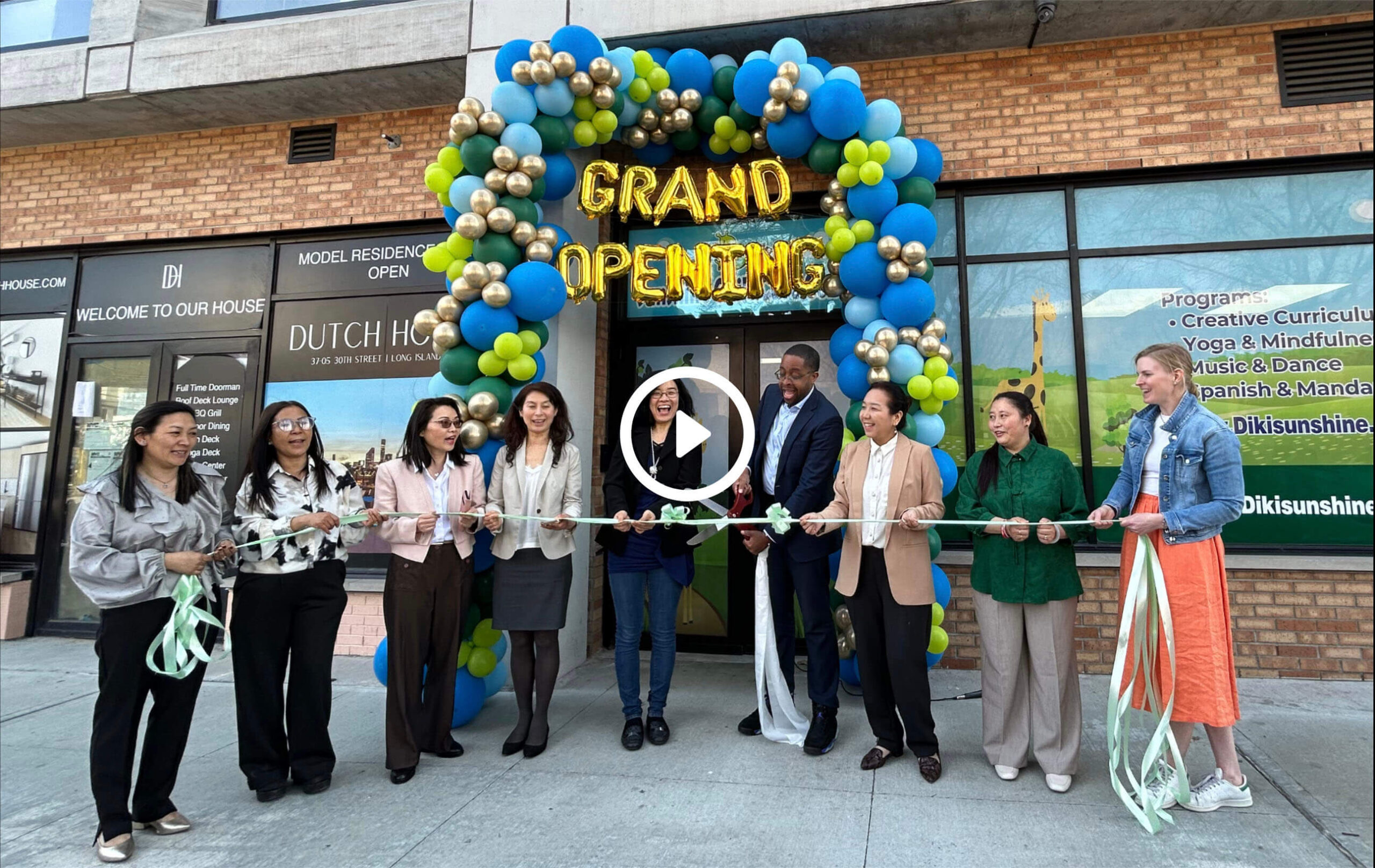 Several people stand in front of the balloon-decorated doors of Diki Sunshine Childcare Center and cut a ceremonial ribbon.