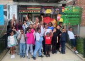 Youth and staff gather outside Oceanside Cornerstone Community Center during their Juneteenth celebration. Some are raising their fists. Banners are behind them.