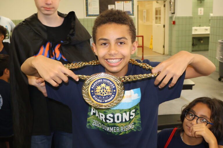 A smiling eighth grade boy wears a medal on a gold chain; the medal says, "Parsons Summer Rising Winner."