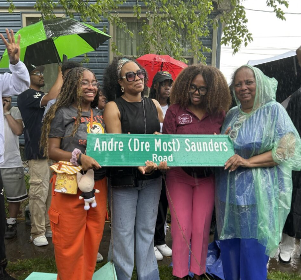 Penny and her family and a councilwoman stand in the rain holding a street sign.