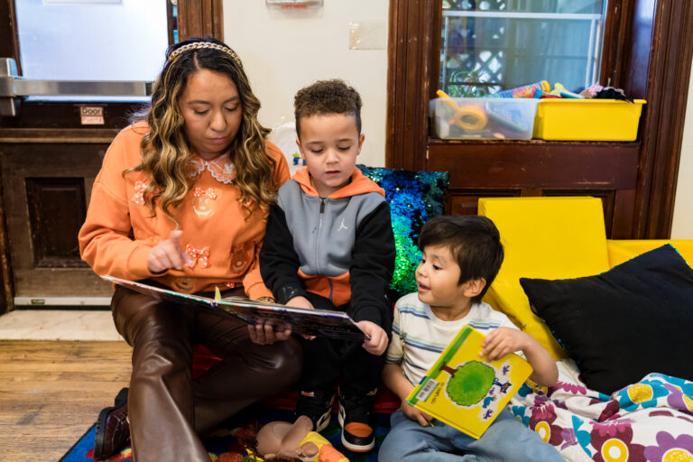 A teacher in a Head Start classroom reads to Saint and another boy.