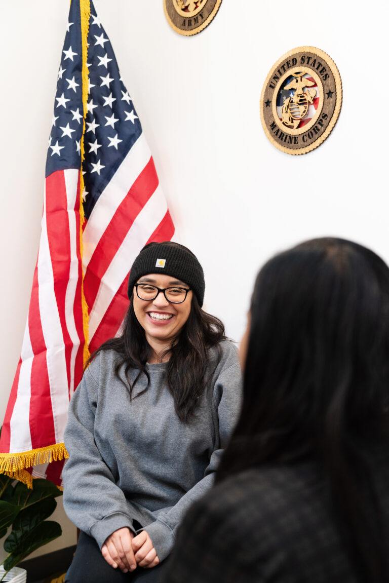 Christie, a client of Military Services, sits smiling with an American flag behind her.